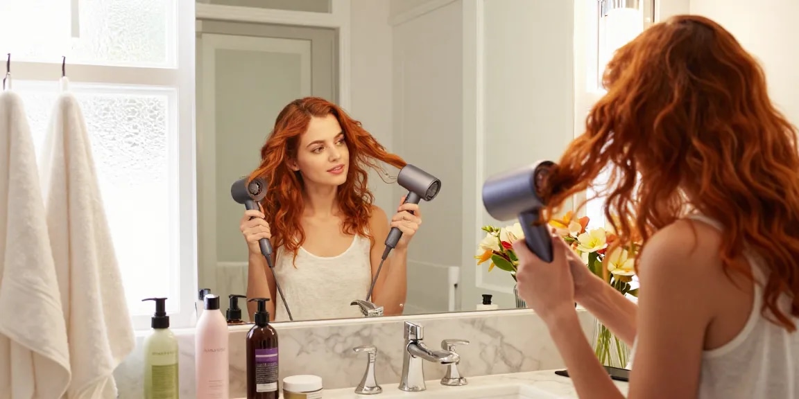 Woman using a mini blow dryer in a chic bathroom for stylish hair.